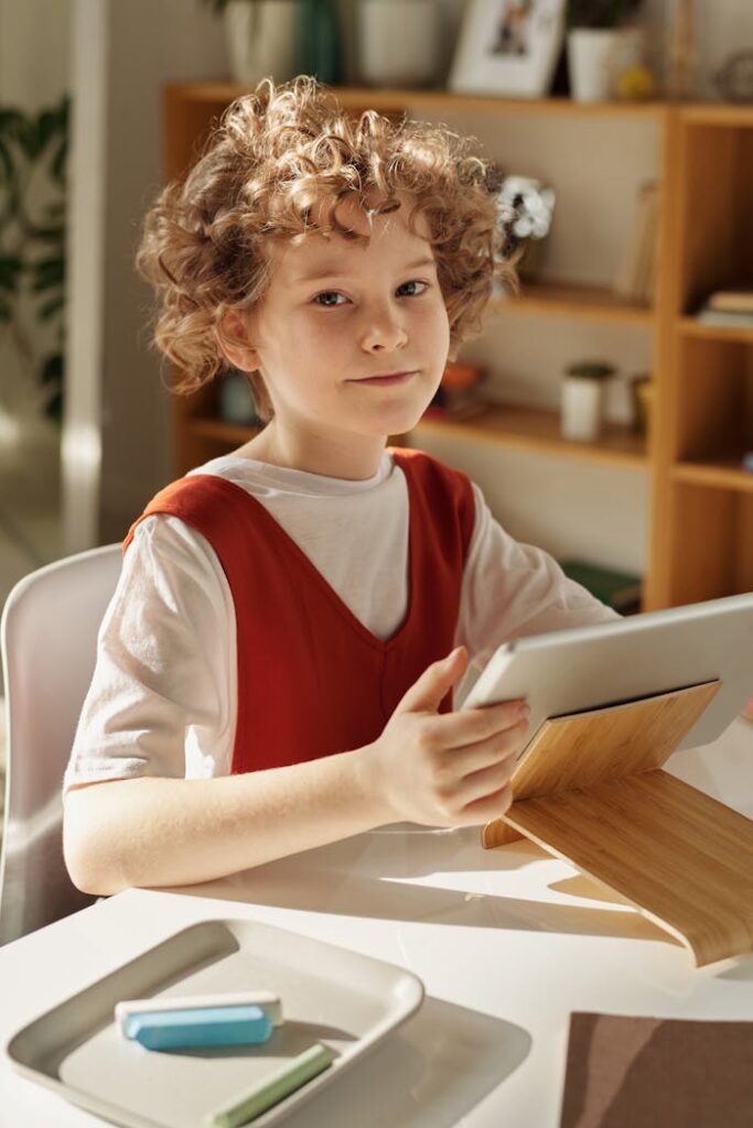 Curly-haired girl using tablet for online learning at home, sitting at desk.